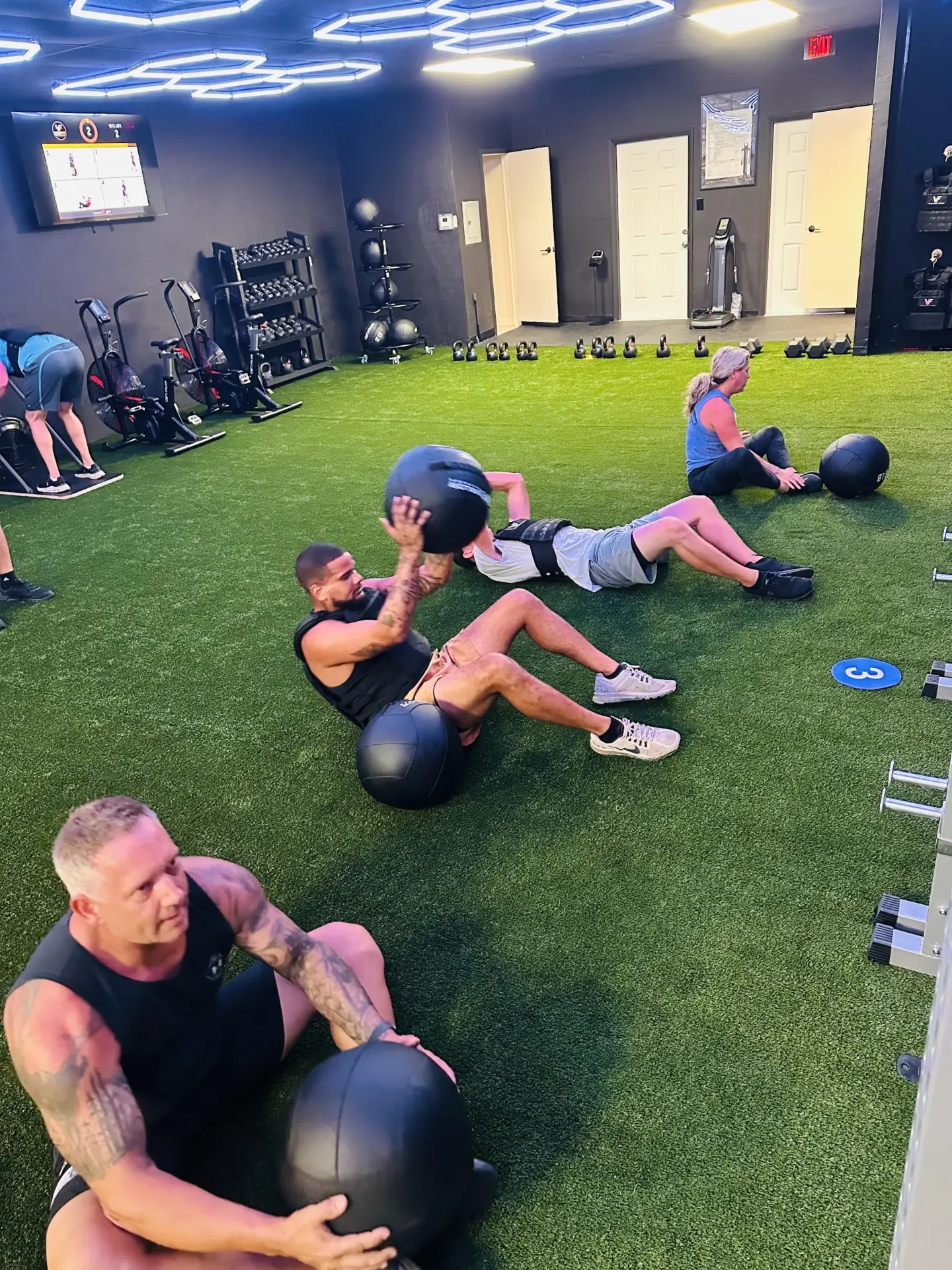 VestFit class doing medicine ball sit-ups together on the turf floor.