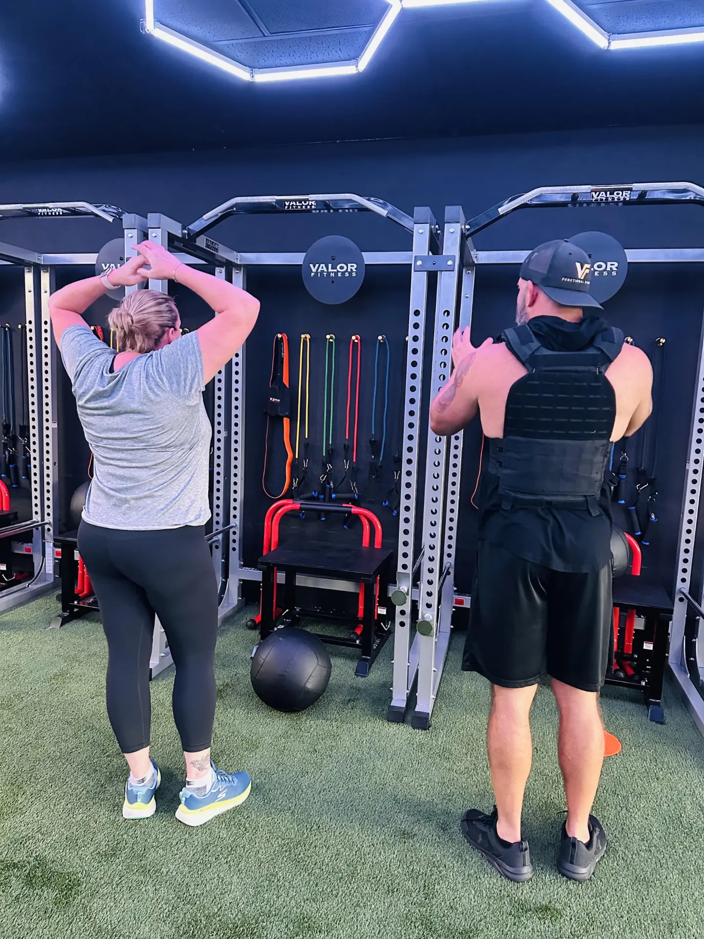 VestFit trainer in a weighted vest coaching a member through a rack workout.