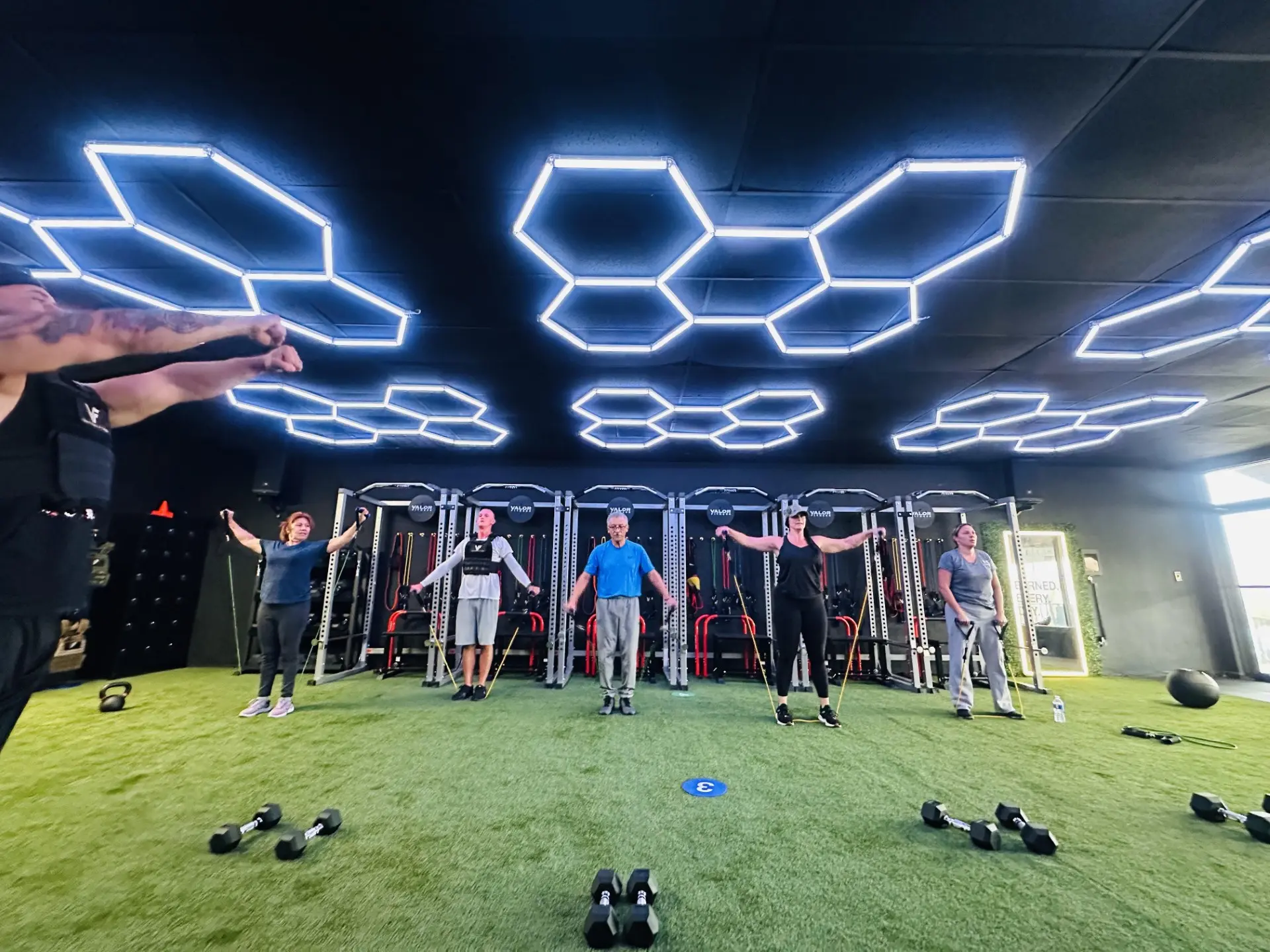 VestFit class training with resistance bands on the turf floor under the studio's hex lights.