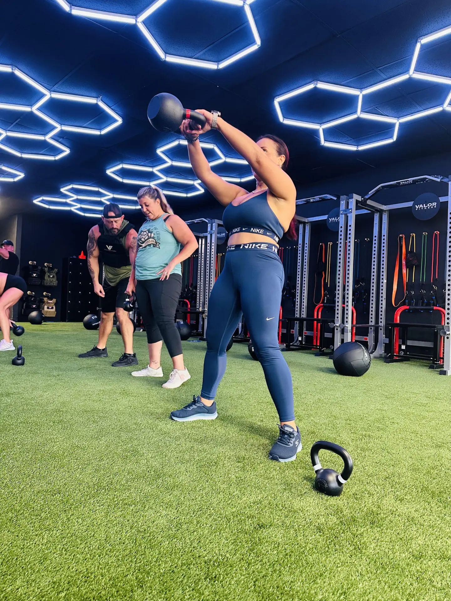 VestFit member swinging a kettlebell overhead on the turf floor during class.